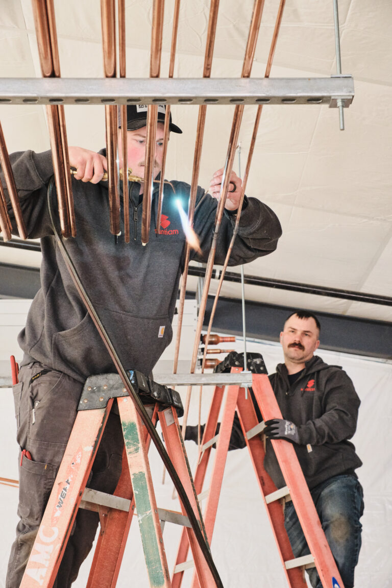 Two technicians working on copper piping from ladder
