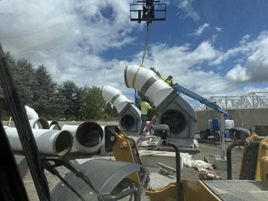 Crane lifting large fiberglass duct section into place at a treatment plant construction site