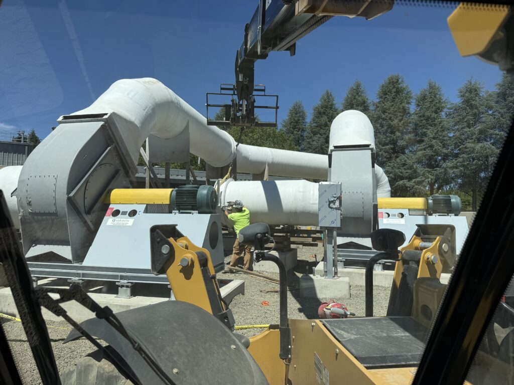 Fan and fiberglass duct assembly being positioned by crane against a blue sky